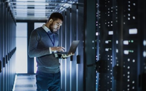 IT Technician Works on Laptop next to a Server Cabinet in Big Da